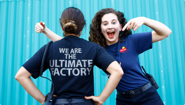 A woman pointing to another woman's back where it's written: We are the ultimate factory